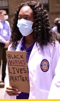 Image of a cardboard sign that reads black nurses lives matter held up to the LSU School of Nursing building sign.