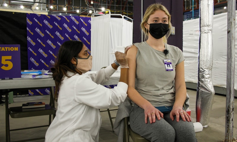 A masked LSU Health New Orleans Allied Health student receives a COVID-19 vaccine from a vaccination clinic staff member wearing a white lab coat.