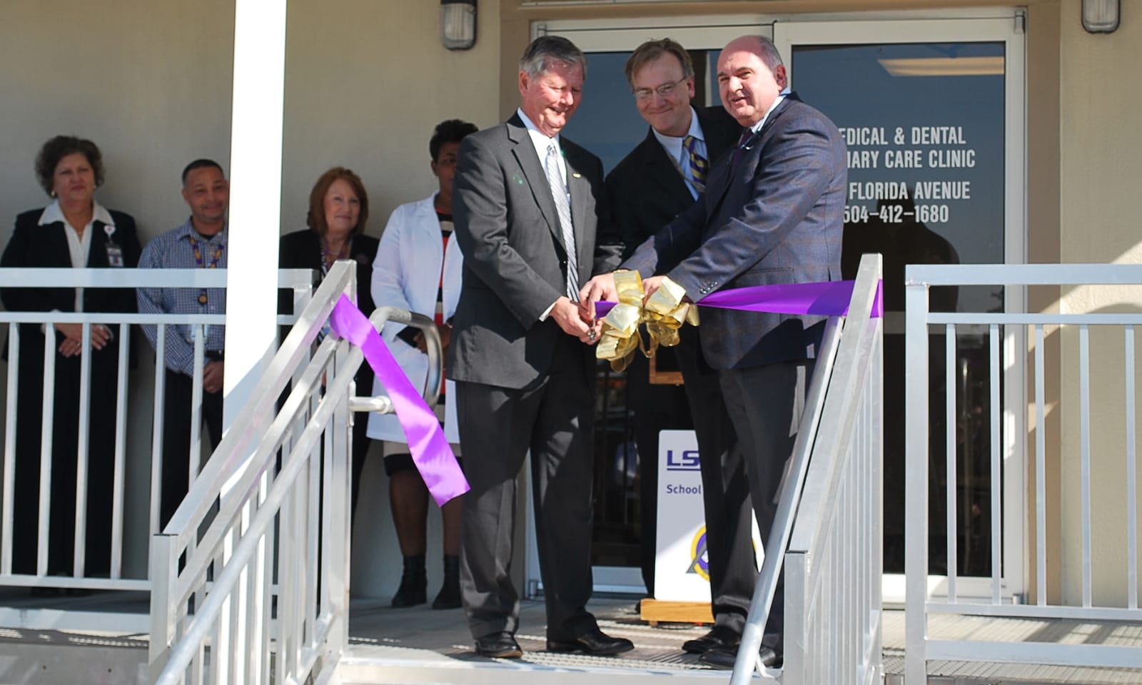 People in suits cut a ribbon in front of a clinic.