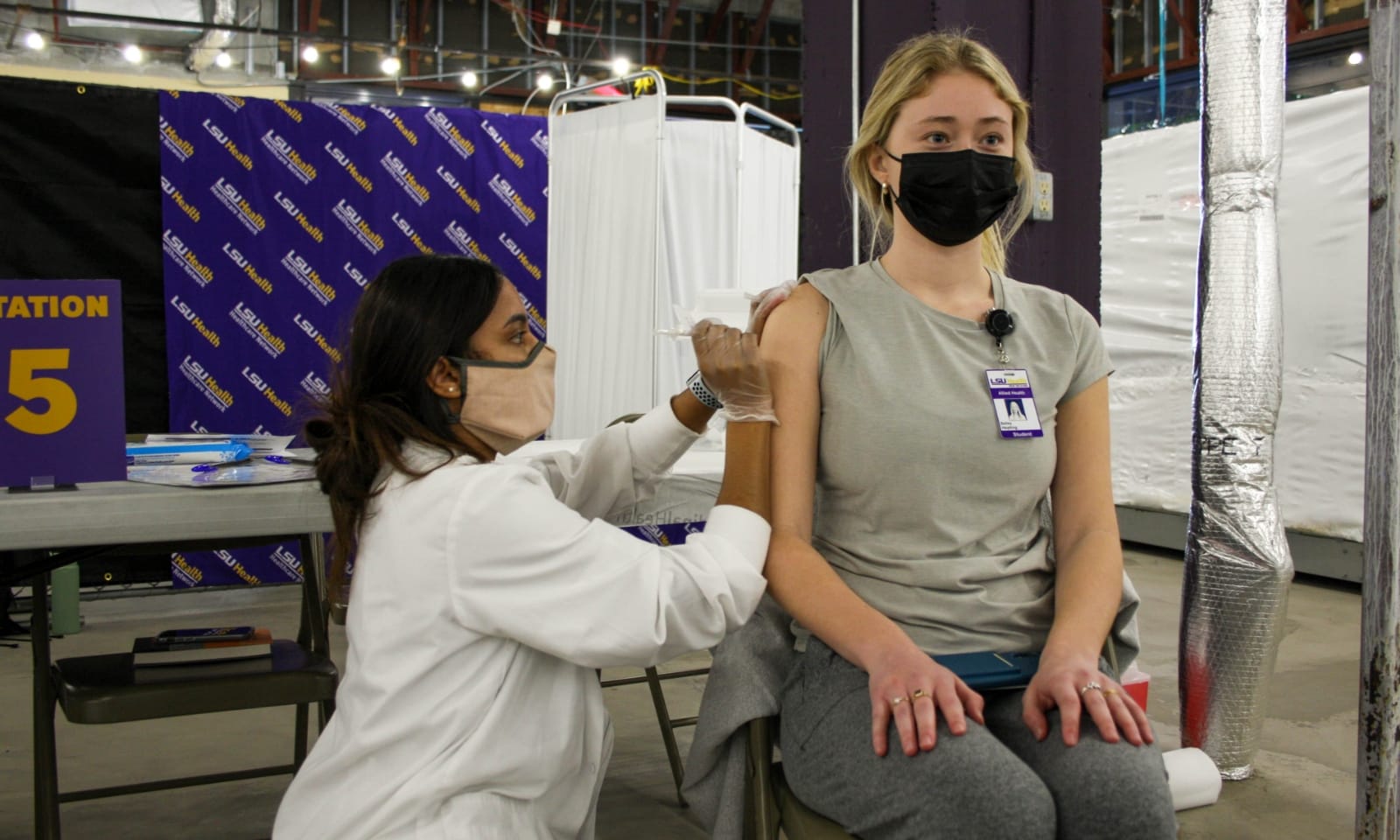 A nurse administers a vaccine to a woman in a mask.
