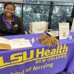 A young woman wearing a black LSU jacket smiles at a purple LSU table.